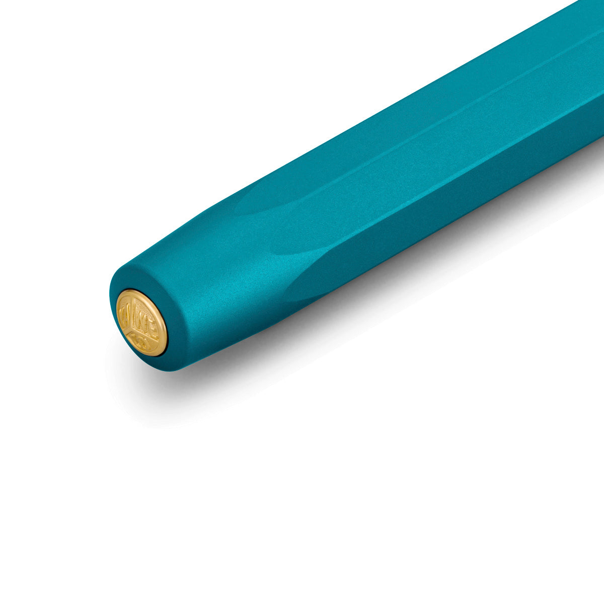 Close-up of the cap of a blue-green pen with a circular gold emblem containing the 'Kaweco' logo on the top.