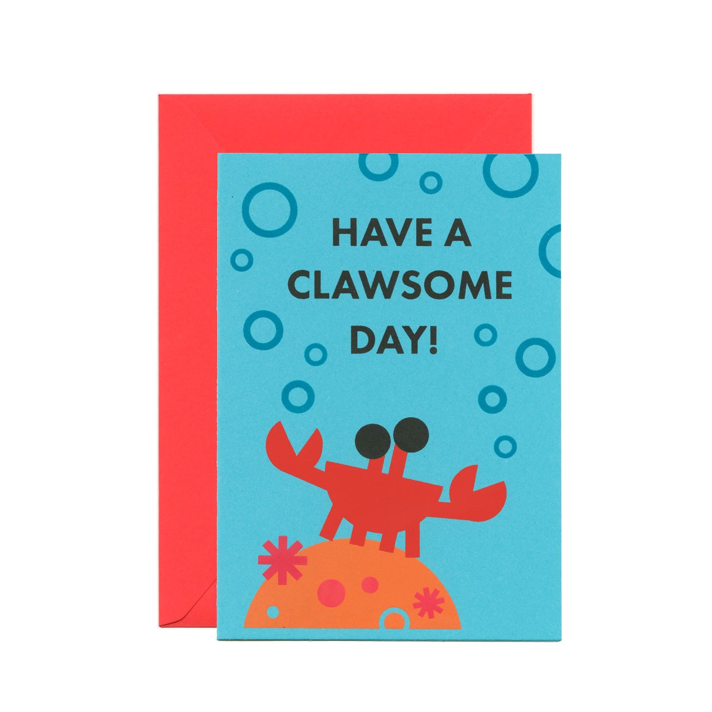 A blue greeting card with an illustration of a crab standing on coral surrounded by bubbles and a text says "Have a clawsome day!". There's a red-pink envelope behind the card.