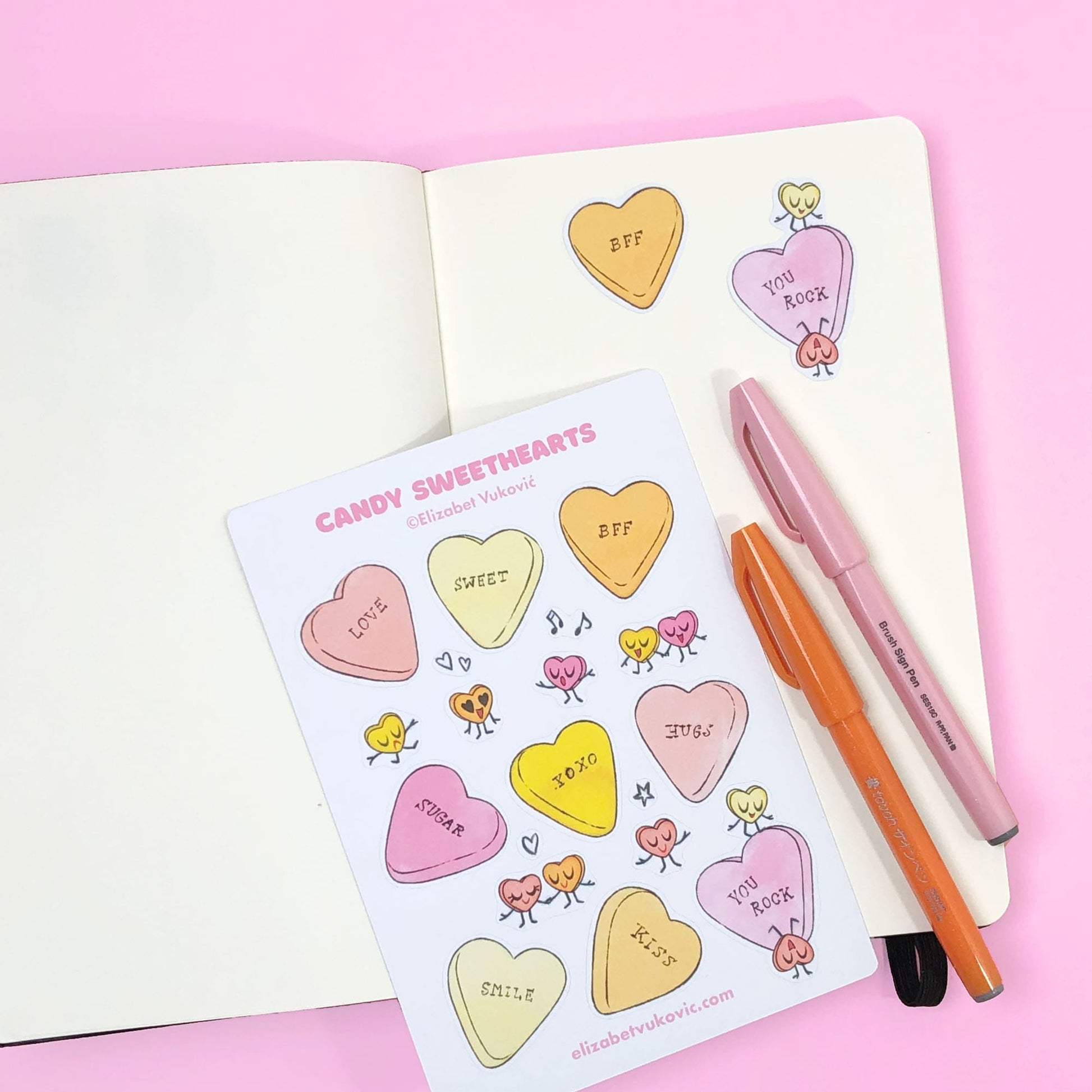 Candy Hearts Pastel Stickers on a notebook with two pens.