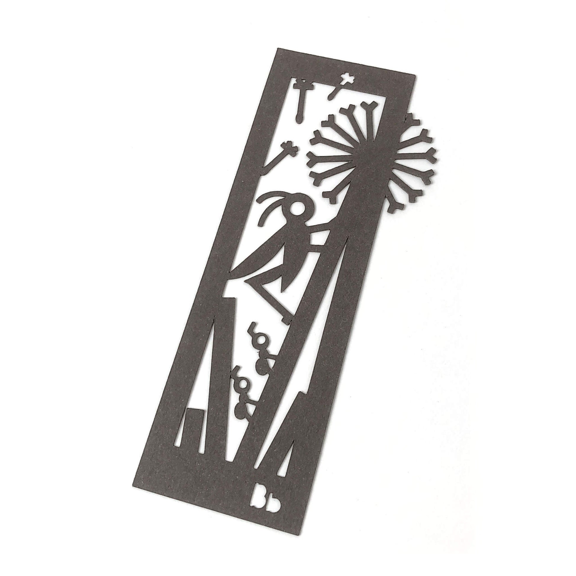 A dark brown paper bookmark with cut-outs of a cricket, ants, dandelion, and seeds surrounded by blades of grass on a white background.