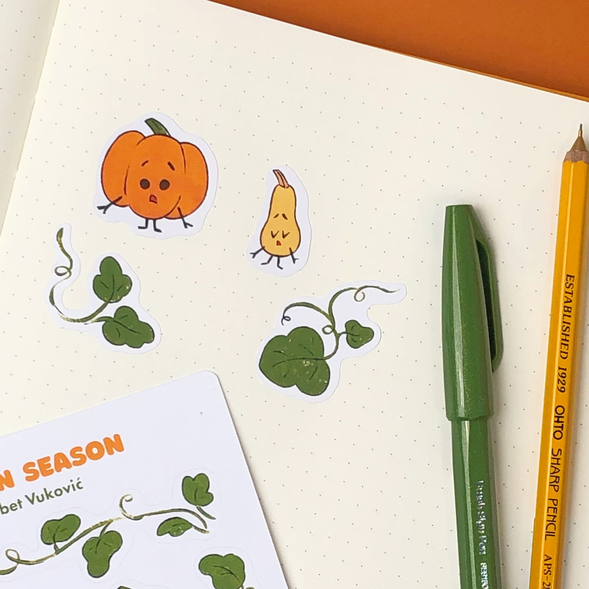 Pumpkins stickers on a notebook page beside it sit a pen and pencil.