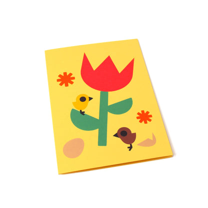 A yellow greeting card with an illustration of a tulip, flowers, eggs, and two chicks, one brown and one yellow.