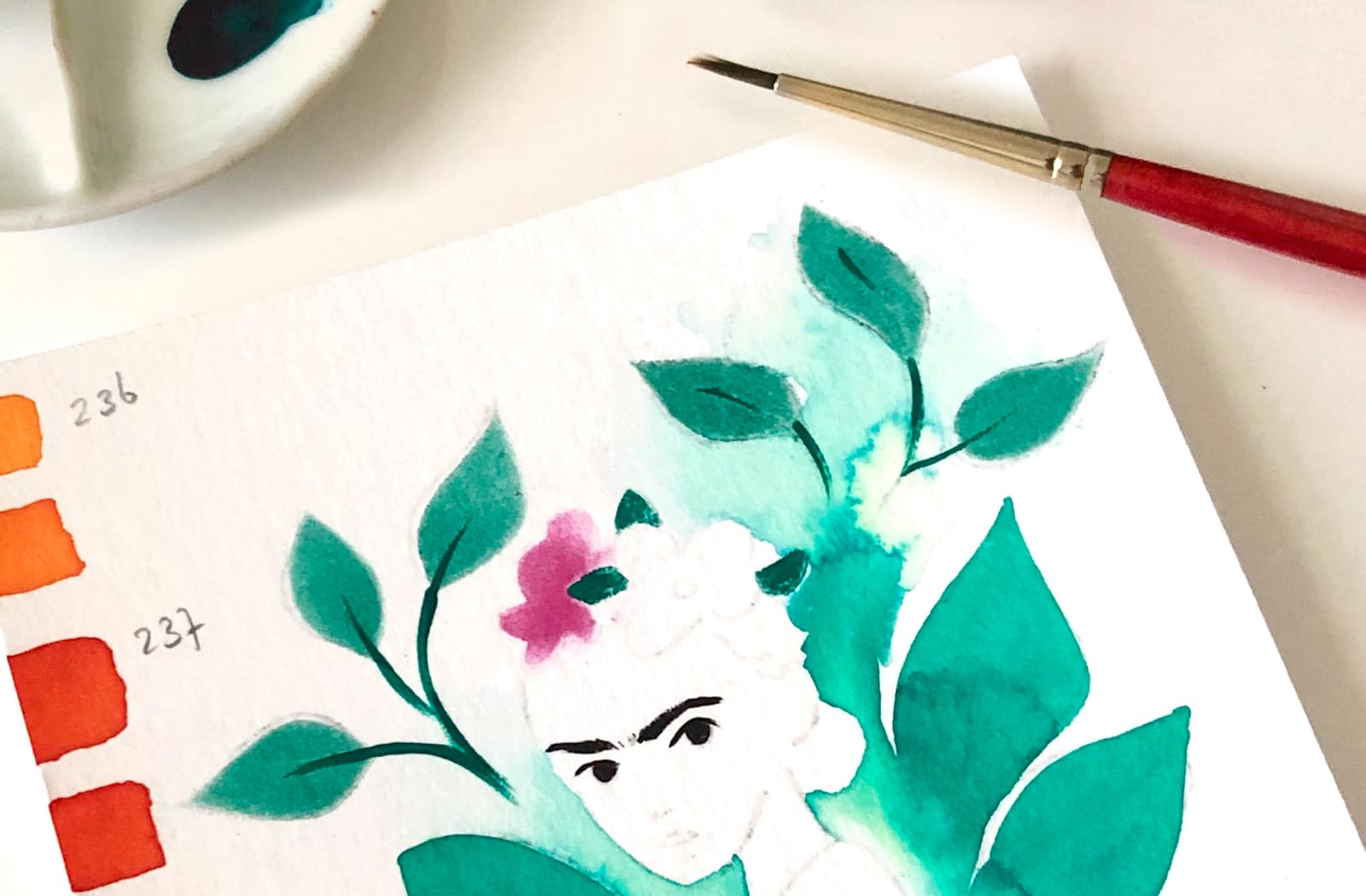 An unfinished illustration of Frida Kahlo surrounded by leaves also a brush and cropped ceramic palette is visible.