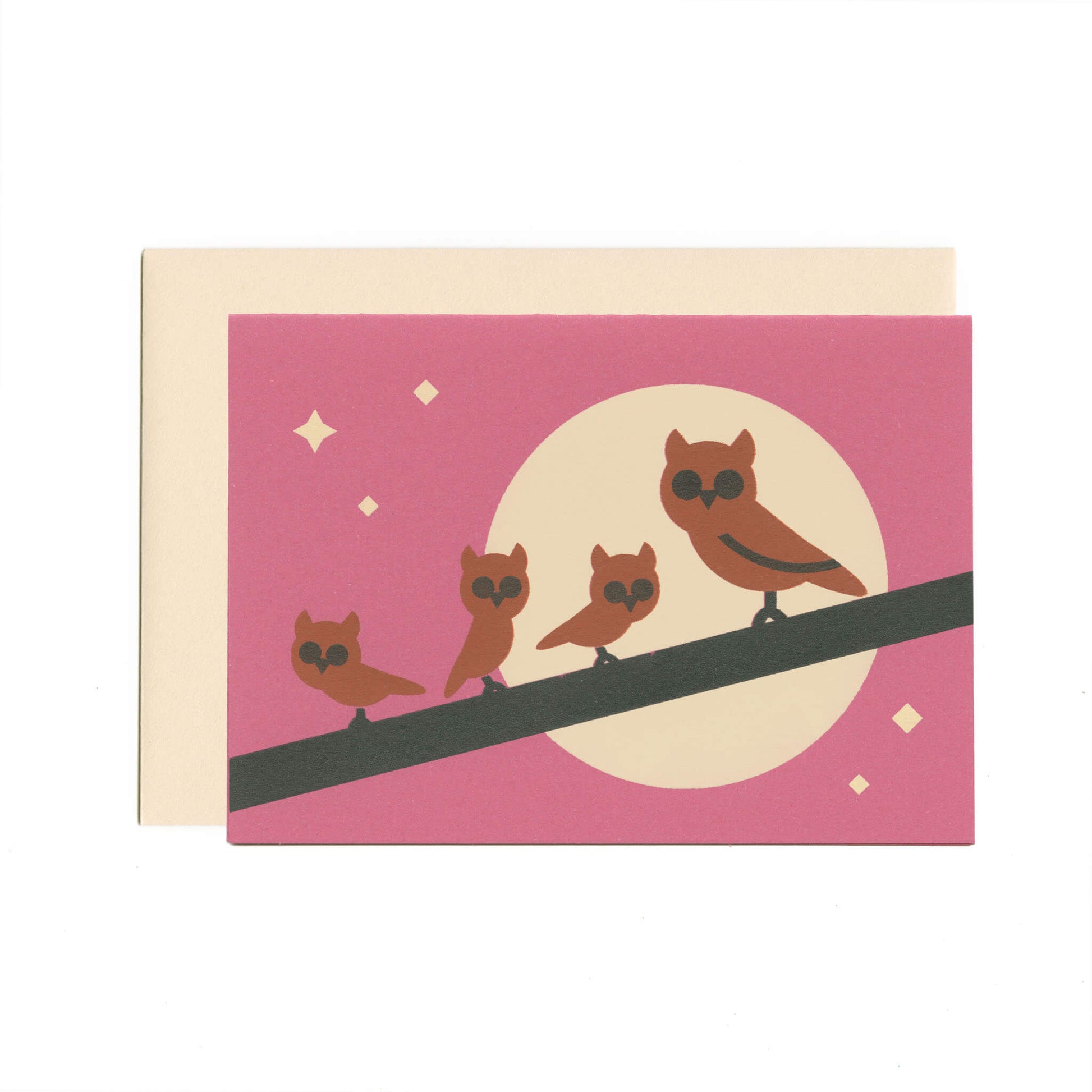 A purple greeting card featuring an illustration of one large and three small brown owls perched on a branch, with a moon and stars in the background. Beneath the card is a beige envelope.