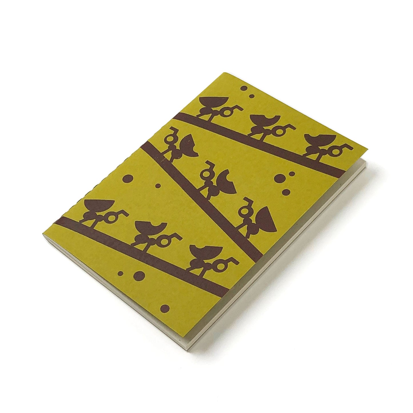 Tilted green notebook with design of dark brown silhouettes of branches with rows of ants carrying leaves with white pages, all on a white background.